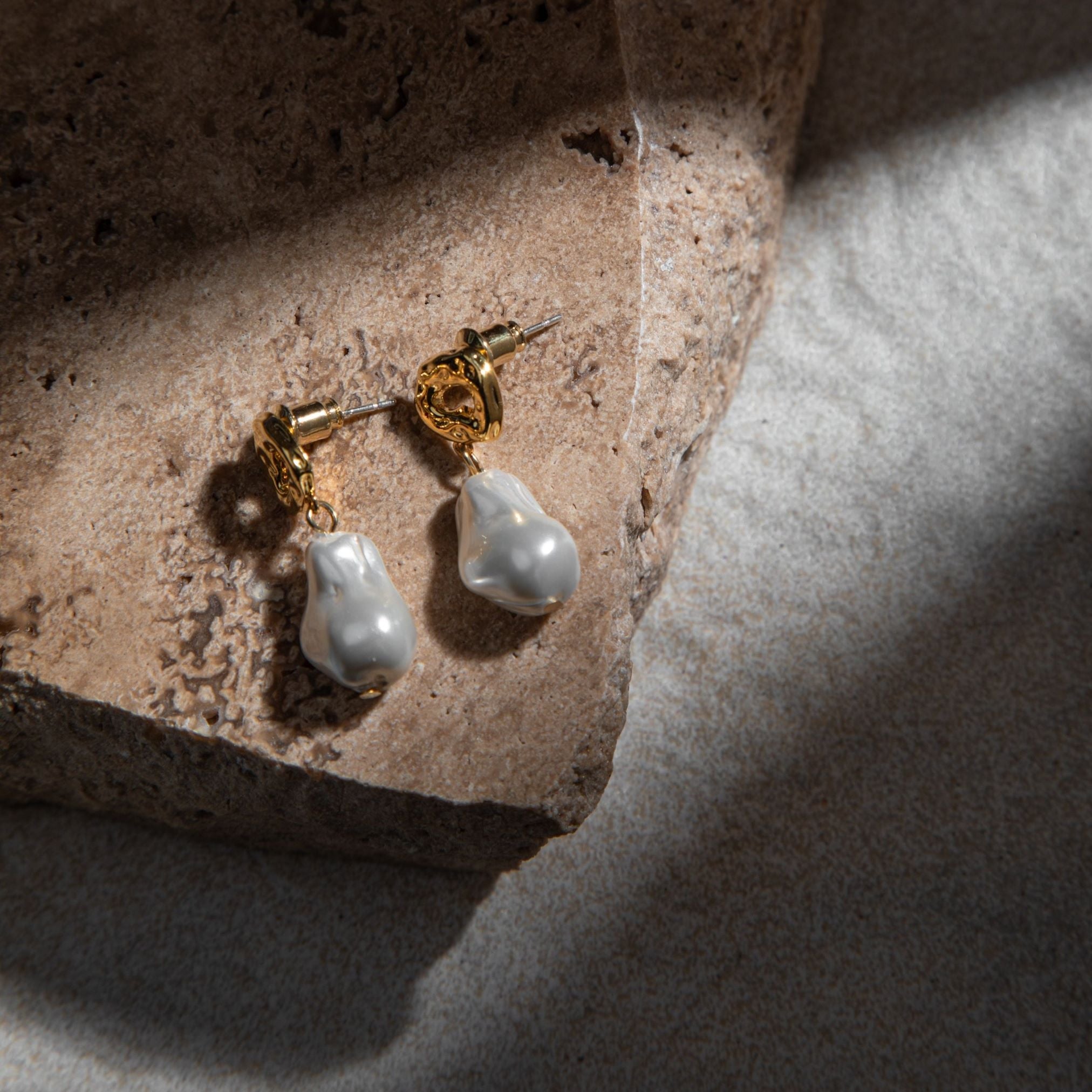 Mini Kat Earrings in gold on textured sandstone paver with mottled grey background in dramatic light