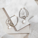 Celeste Earrings – silver knot and pearl drop earrings on white tile background