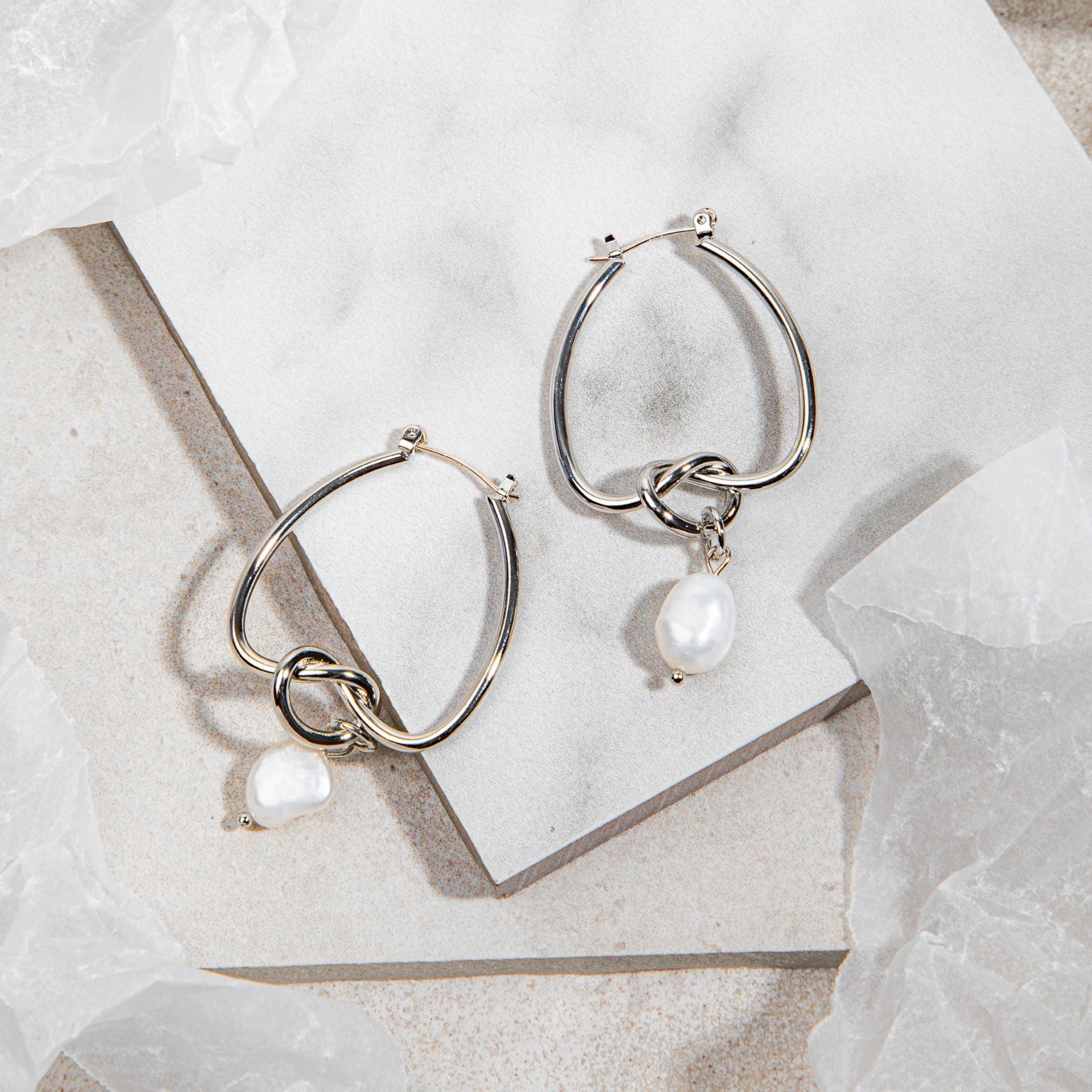 Celeste Earrings – silver knot and pearl drop earrings on white tile background