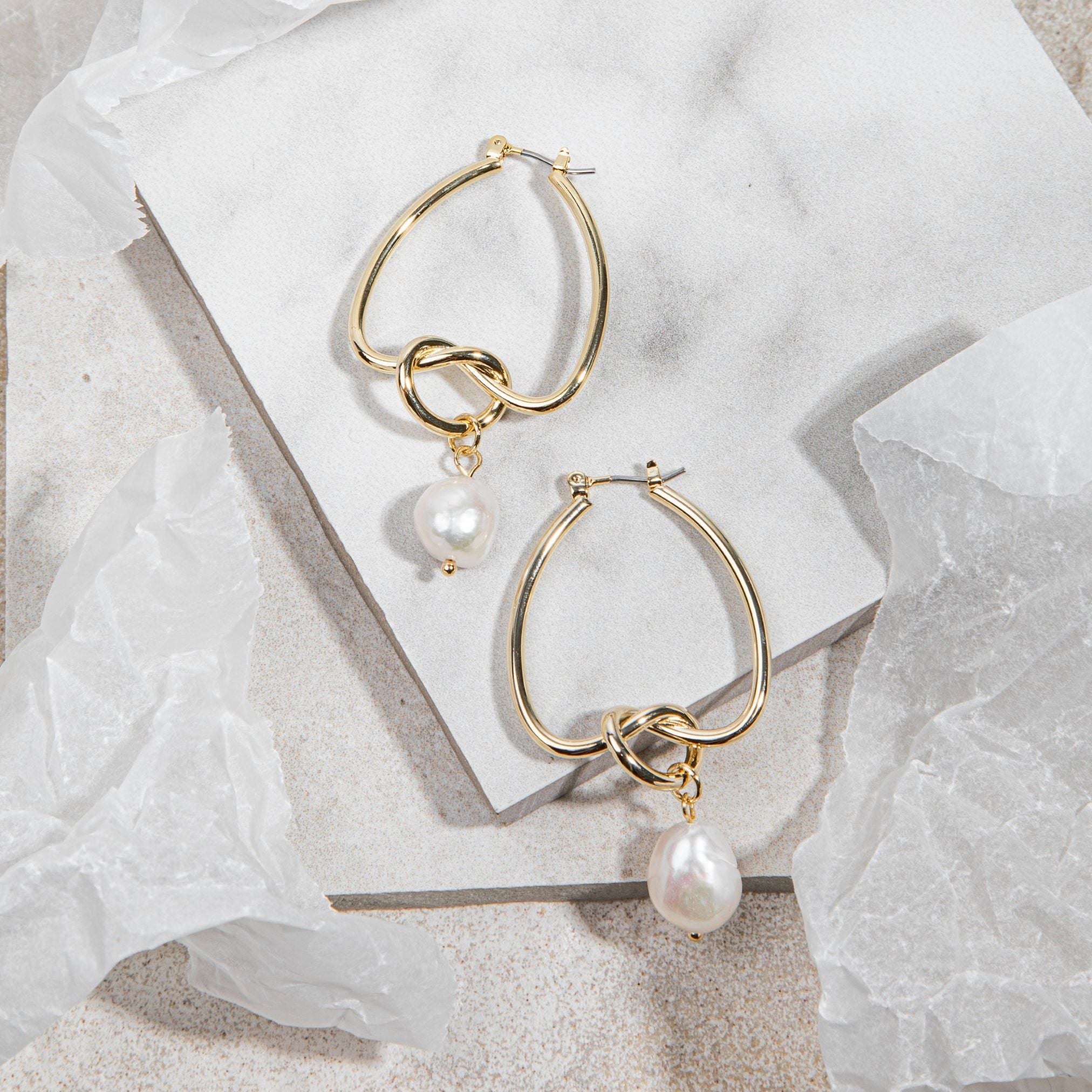 Celeste Earrings – gold knot and pearl drop earrings on white tile background