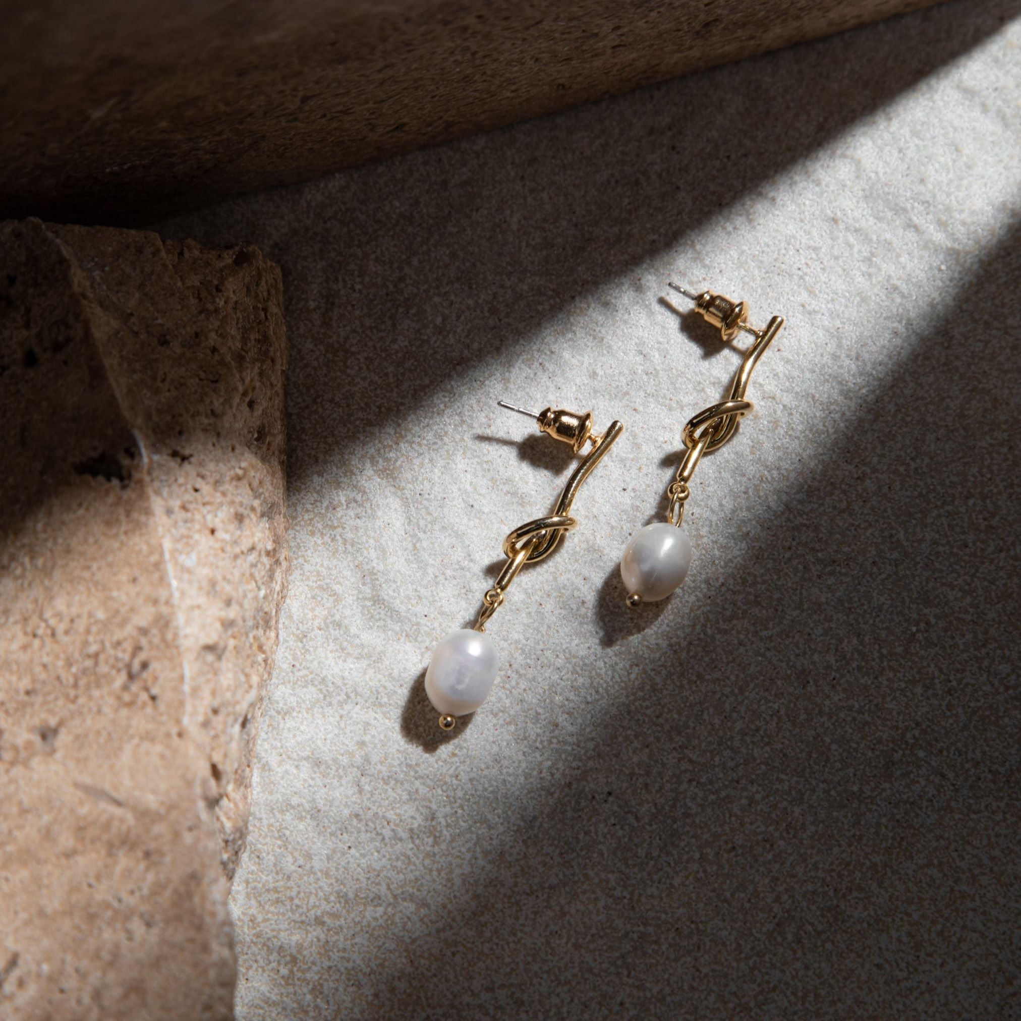 Crystal Earrings – illuminated by dramatic ray of light on mottled grey-brown background with brown pavers