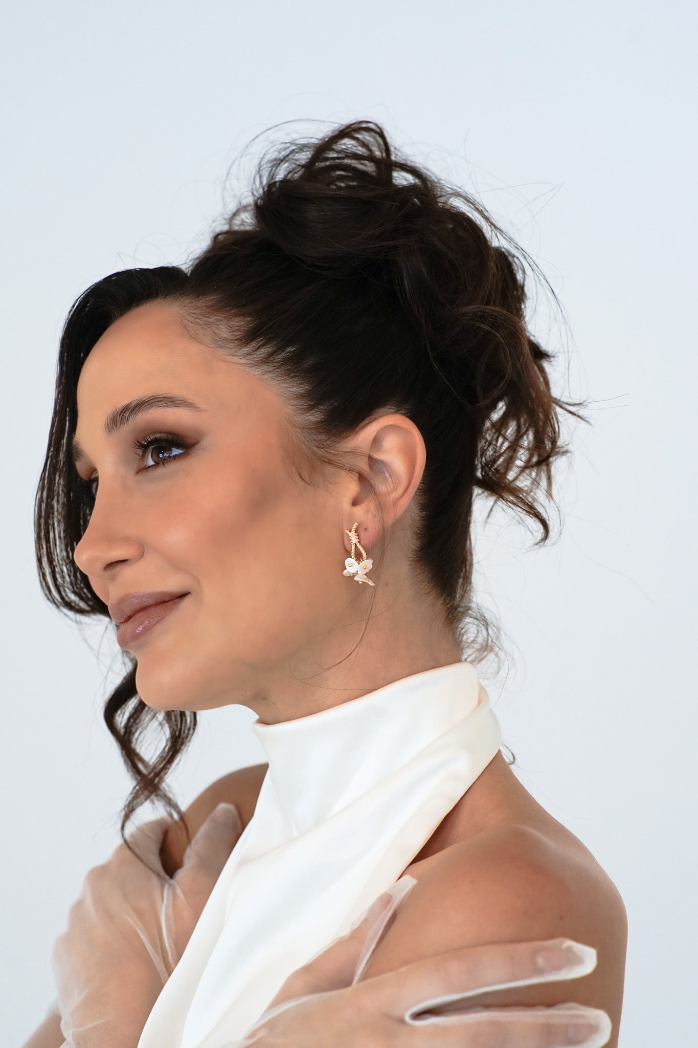 Bride in updo wearing Loretta Earrings – pensive gaze off-camera with gloved hand resting on shoulder