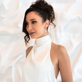 Bride wearing gold Sophia Earrings with hands in front of stomach, soft bridal expression in white textured setting
