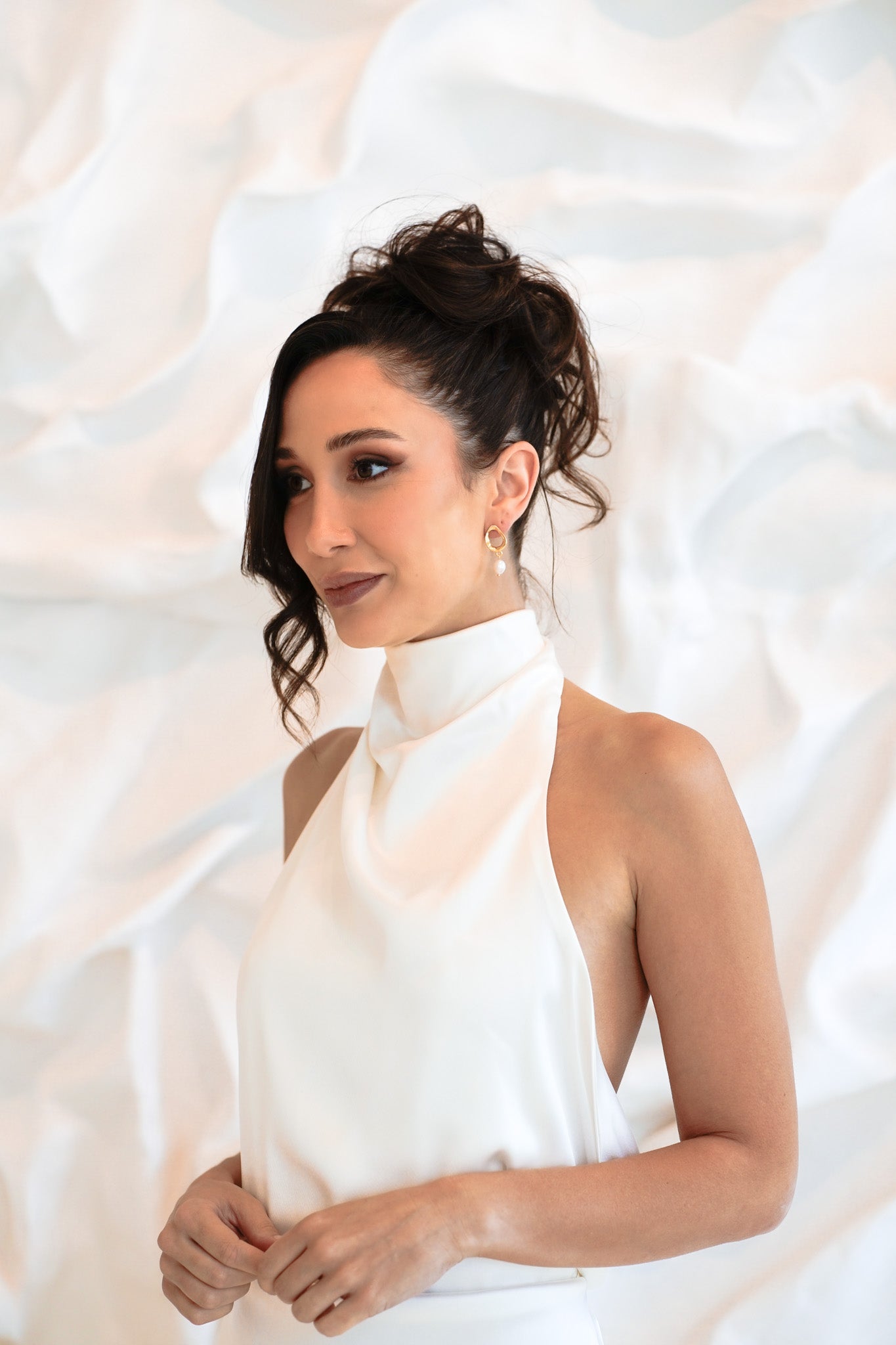 Bride wearing gold Sophia Earrings with hands in front of stomach, soft bridal expression in white textured setting