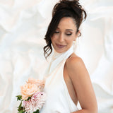 Bride in white halter dress smiling with eyes closed and holding bouquet – wearing gold Sophia Earrings against soft white backdrop
