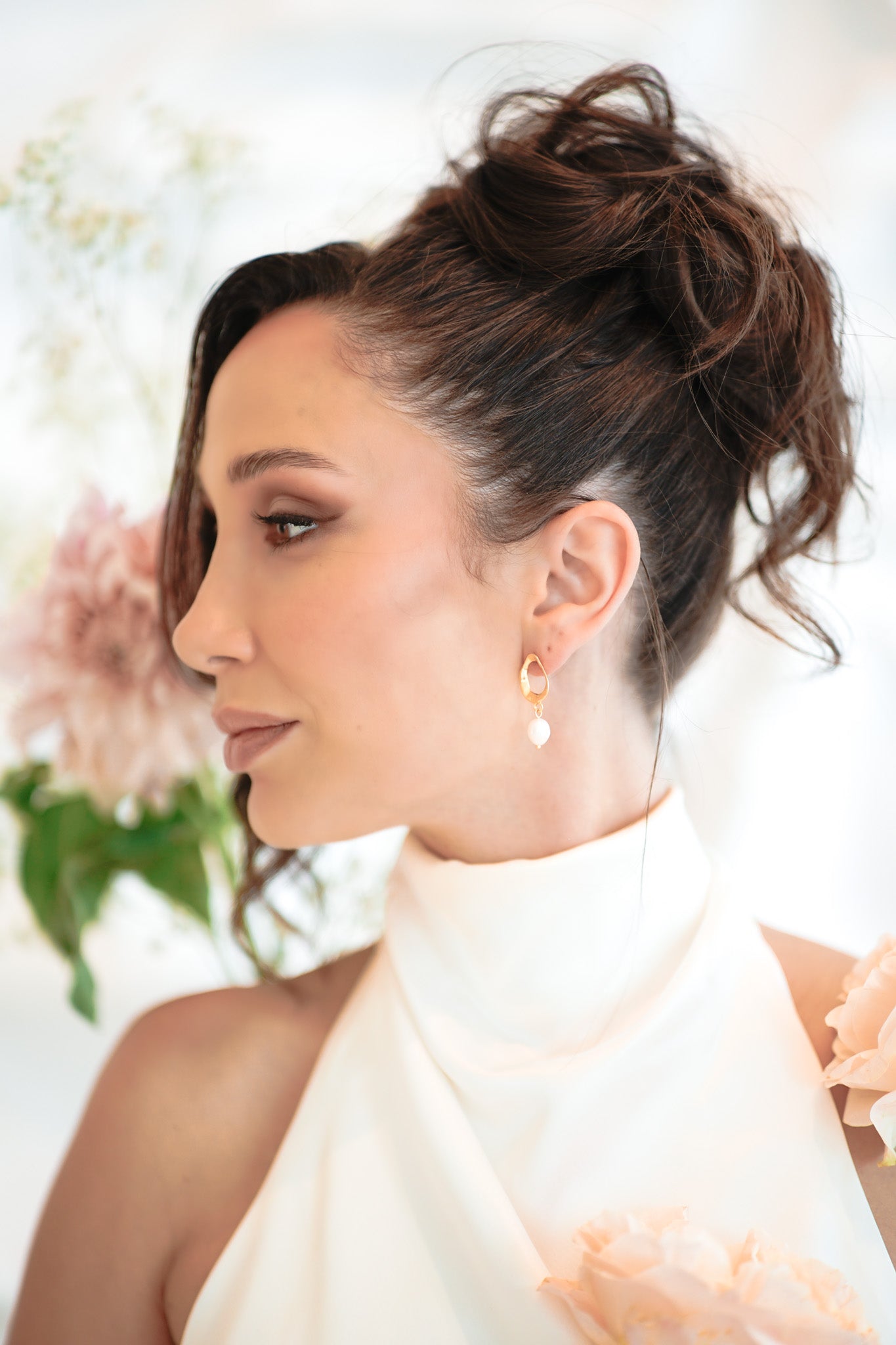 Bride with brunette updo wearing gold Sophia Earrings – soft flower and bridal bouquet in background