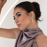 Close-up of woman in purple-grey halter dress wearing Kiera Earrings, looking up with a soft smile – hair in bun, natural bridesmaid makeup