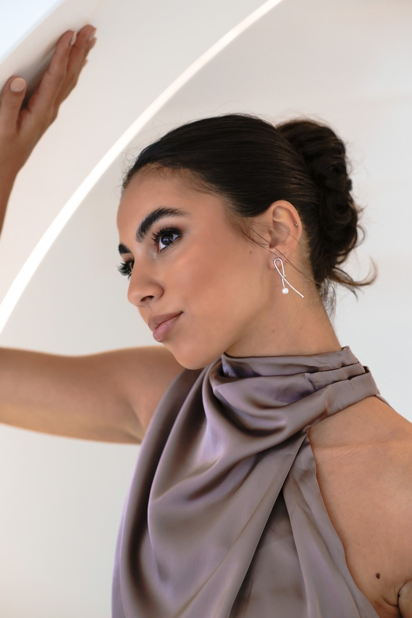 Close-up of woman in purple-grey halter dress wearing Kiera Earrings, looking up with a soft smile – hair in bun, natural bridesmaid makeup
