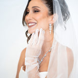 Bride smiling in The Simone Set – matching floral drop earrings and necklace styled with veil and sheer bridal gloves