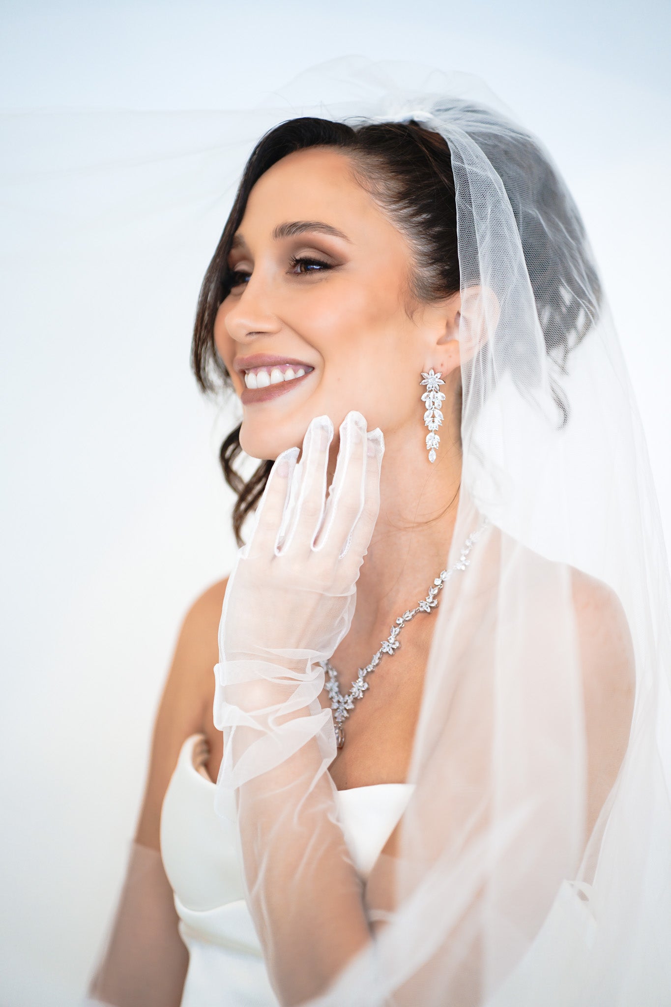 Bride smiling in The Simone Set – matching floral drop earrings and necklace styled with veil and sheer bridal gloves