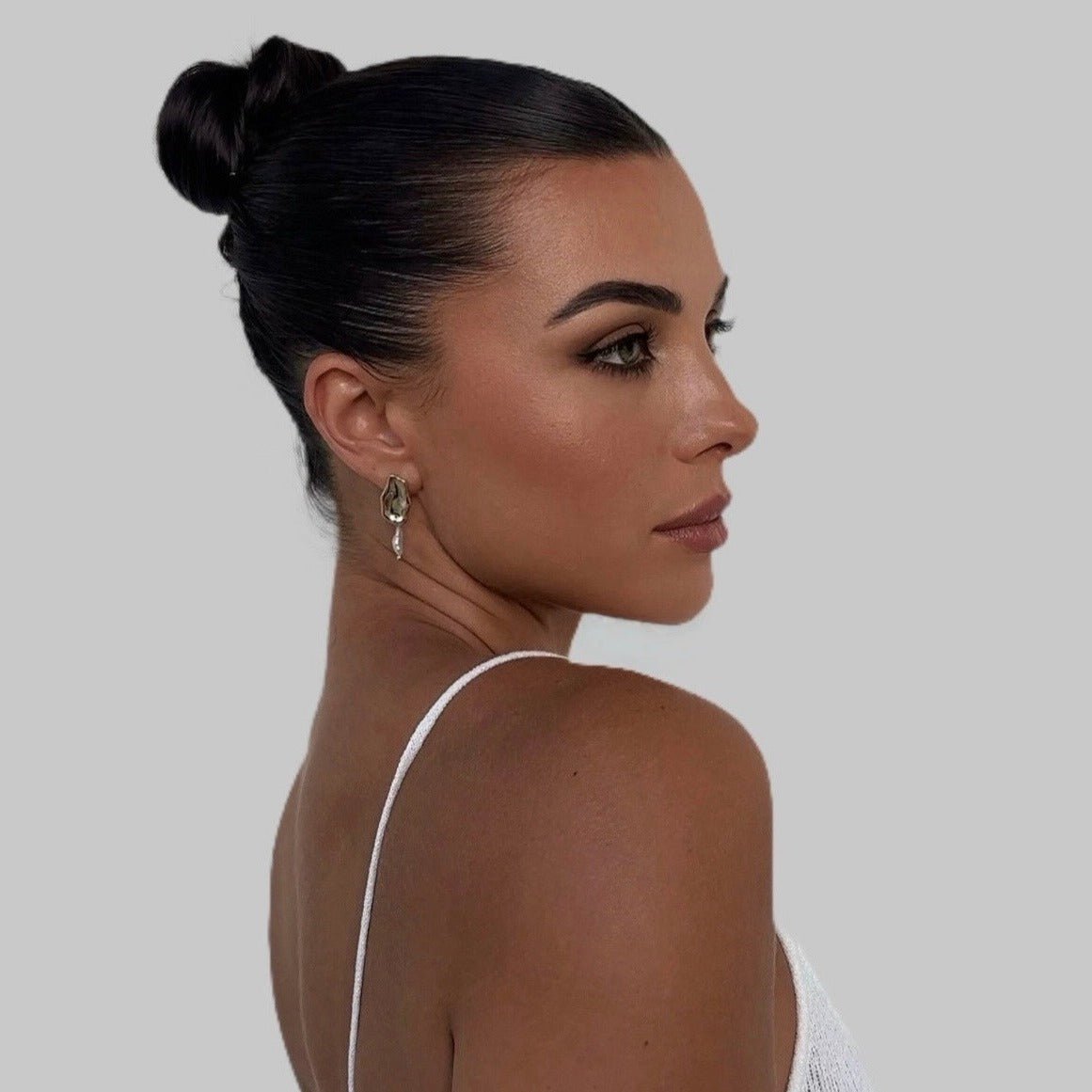 Woman wearing Leah Earrings in profile – black hair in sleek bun, white outfit, confident expression and pearl drop visible against clean skin