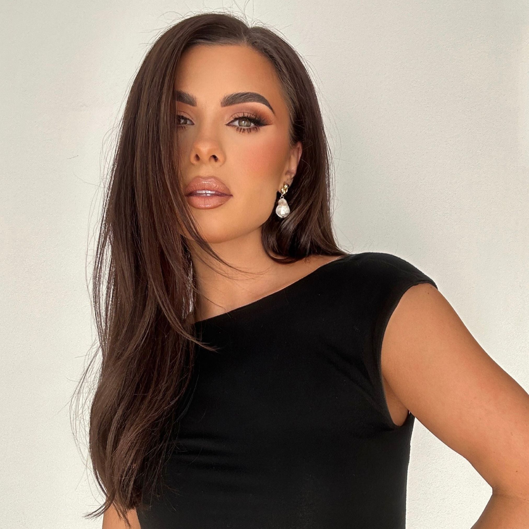 Woman wearing silver Kat Earrings with glossy brunette hair, nude lipstick and blush makeup, black dress and smooth tan skin