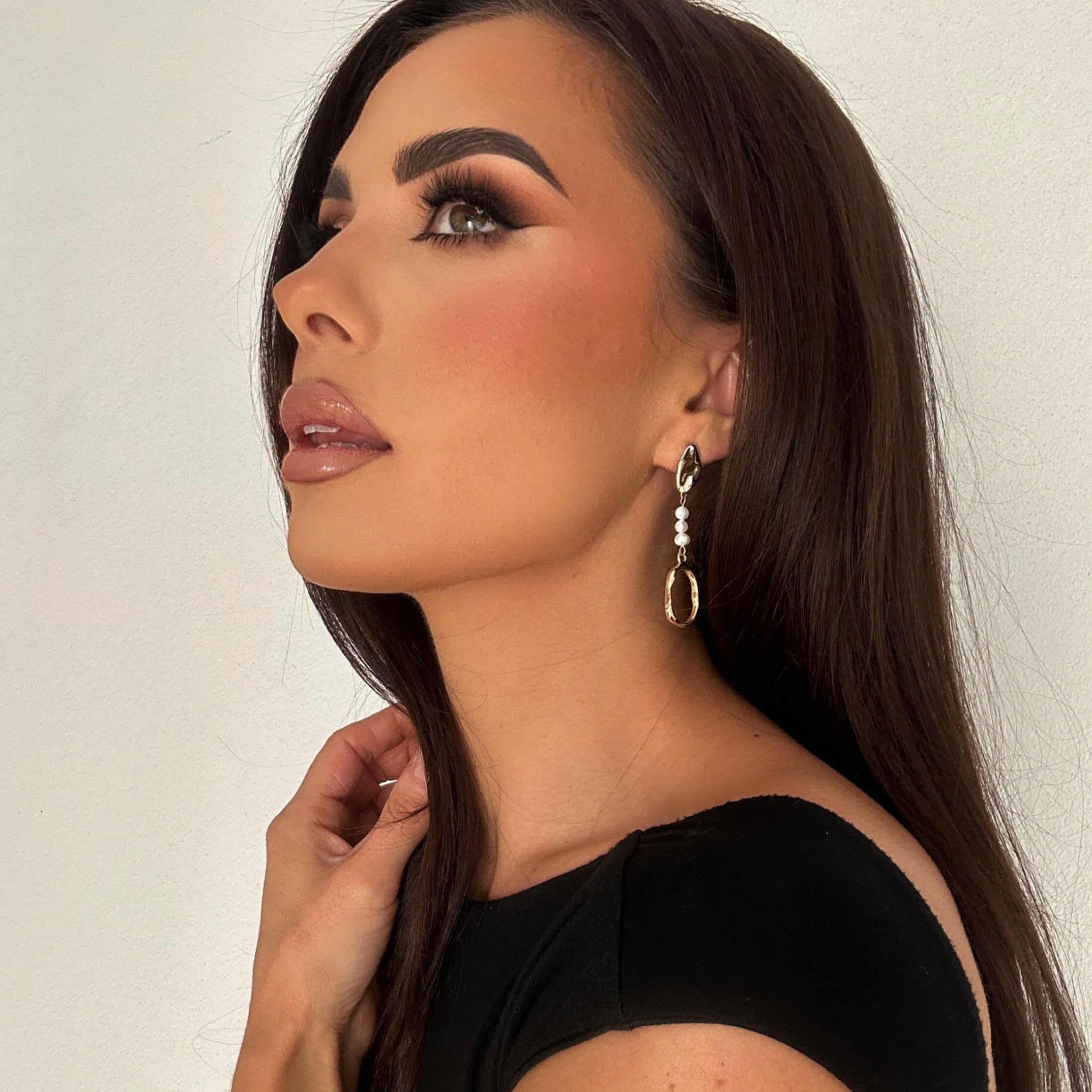 Woman wearing Tania Earrings with glossy brunette hair and soft makeup, gazing upward with a serene expression – highlighting the sculptural pearl drop design