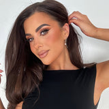 Woman in black dress wearing Kiera Earrings – featuring gold knot and pearl detail, styled with glossy brunette hair and soft makeup