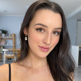 Woman with wavy dark brunette hair wearing Mini Kat Earrings in gold, styled with natural makeup