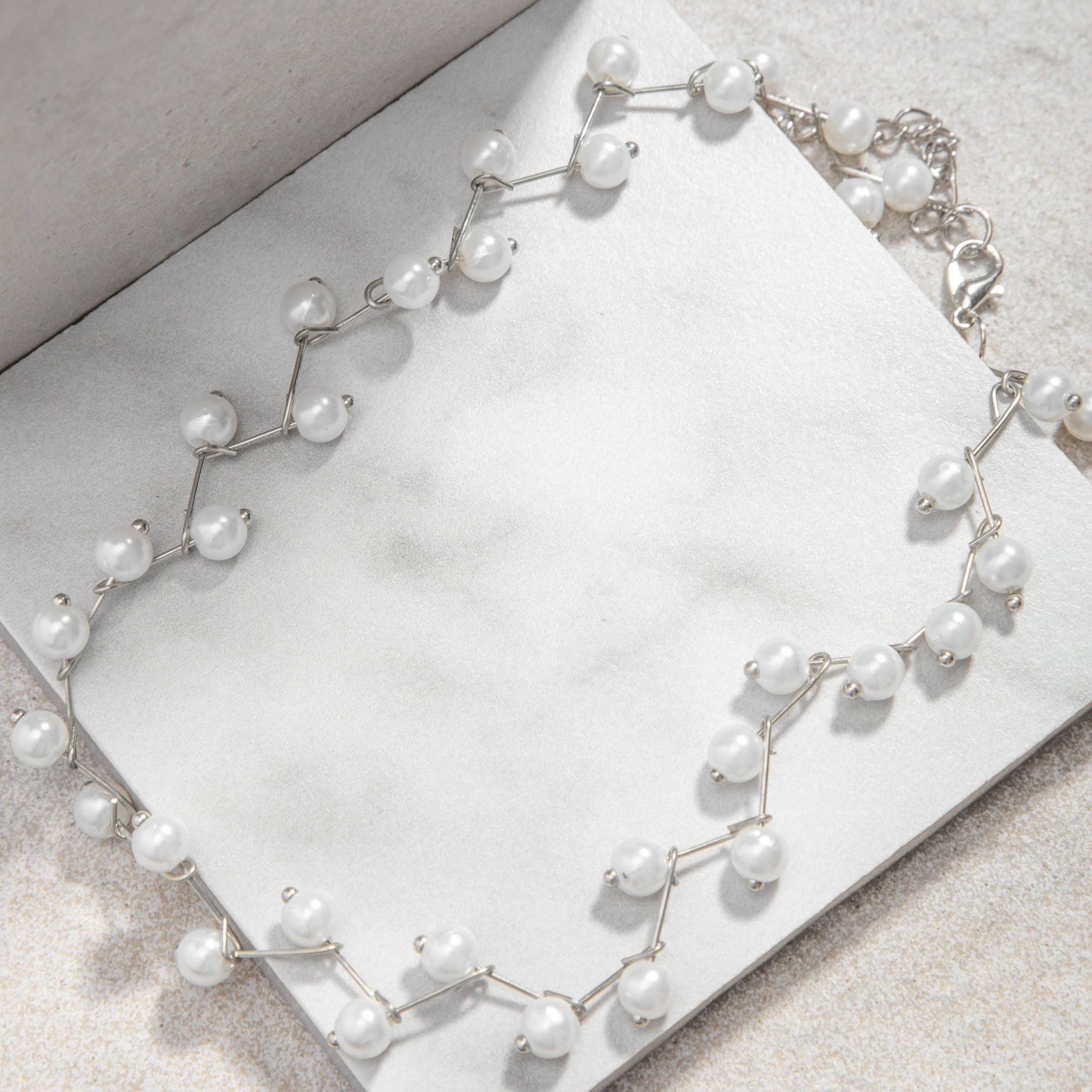 Jana Necklace – gold zig-zag pearl choker on white tile with mottled grey felt background