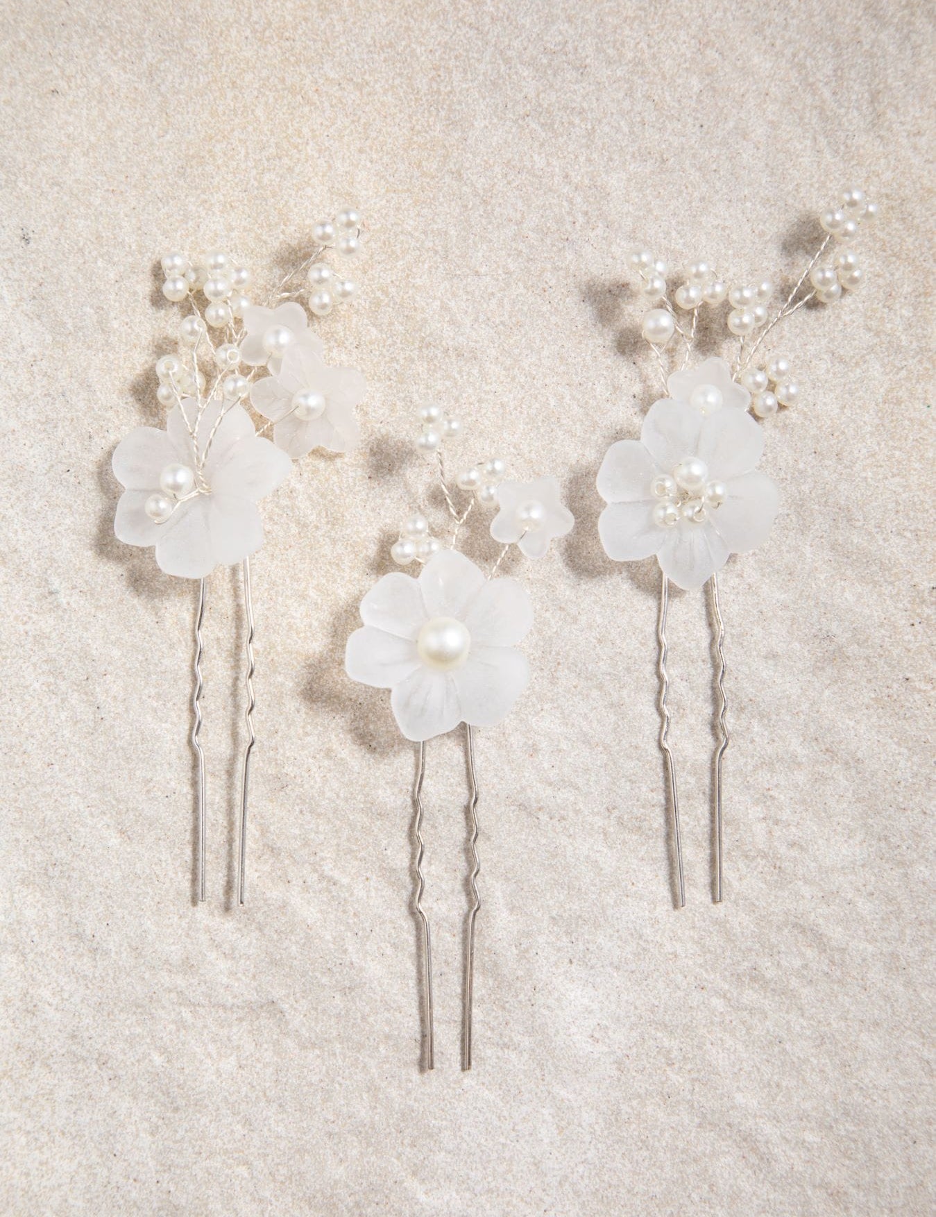 Flatlay of Beth Hair Pins on grey-brown textured background – soft matte white flowers and pearl branches displayed against felt or paper surface