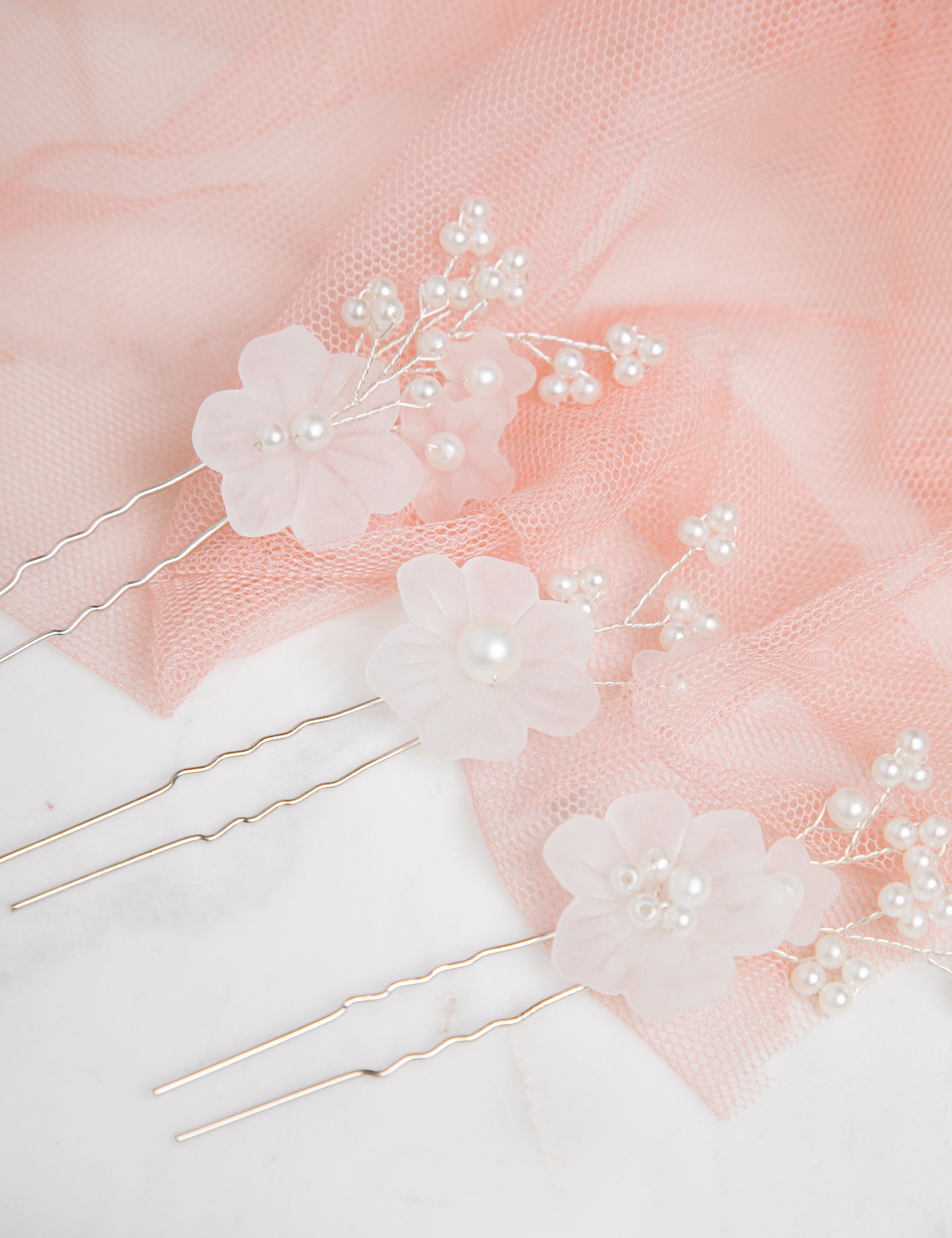 Beth Hair Pins arranged on mesh with warm pink fabric and lace overlay – marble bench partially visible beneath layers