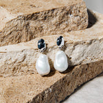 Kat Earrings – freshwater pearl drop earrings in silver on stacked brown pavers and concrete background