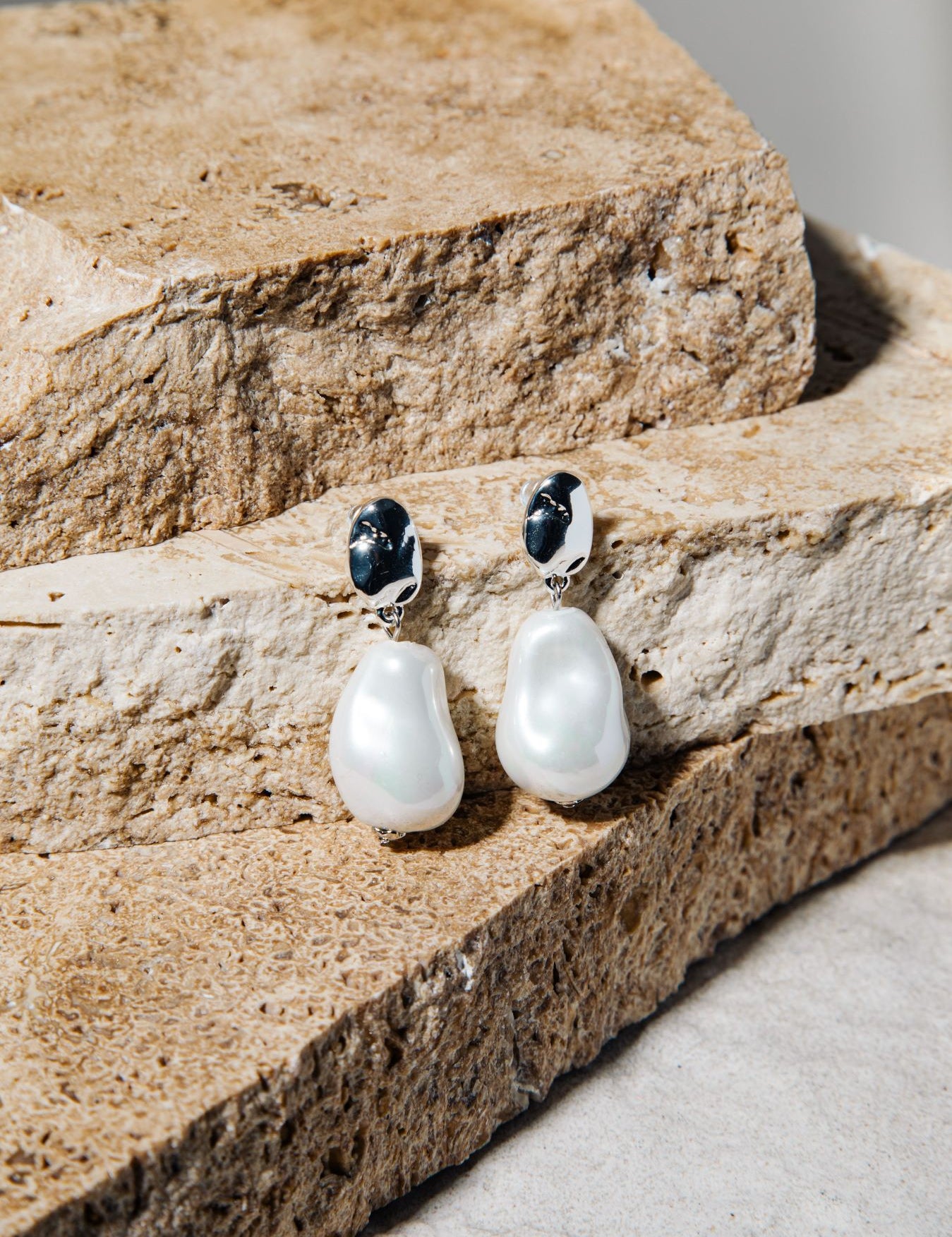 Kat Earrings – freshwater pearl drop earrings in silver on stacked brown pavers and concrete background