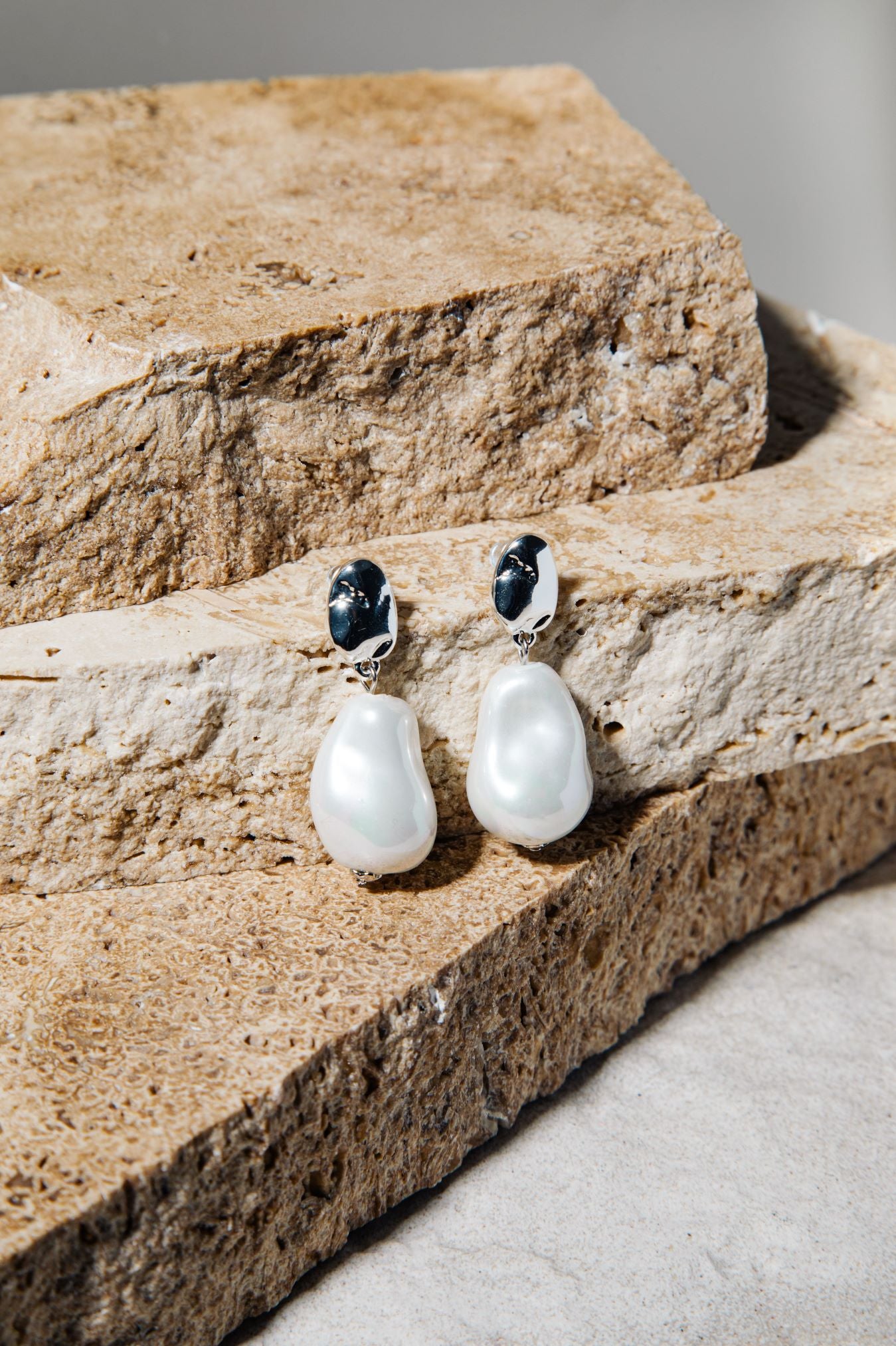 Kat Earrings – freshwater pearl drop earrings in silver on stacked brown pavers and concrete background
