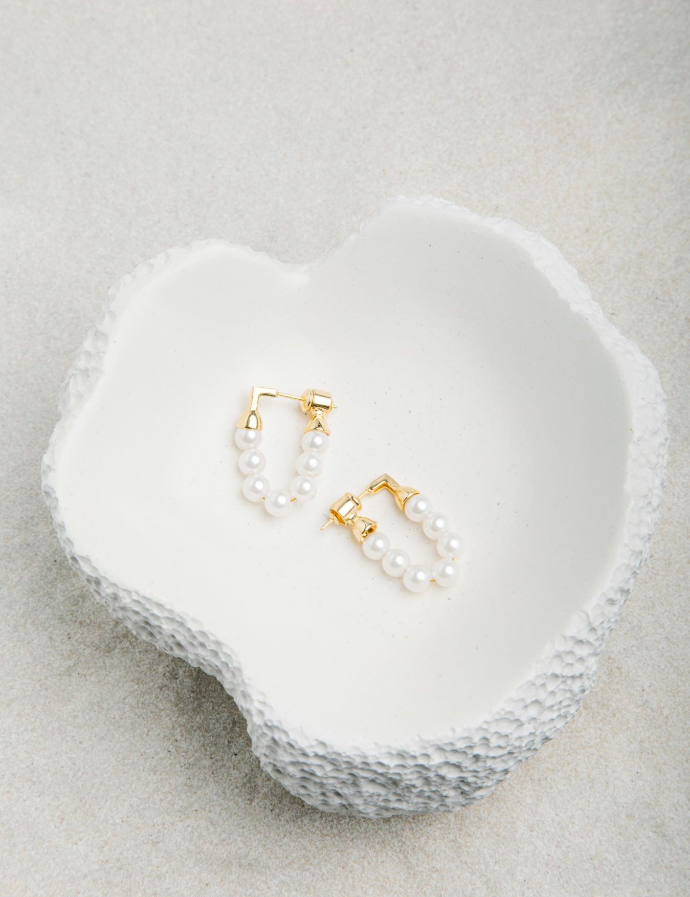 Kristy Earrings displayed in a smooth porcelain bowl with dimpled outer texture, set against a soft felt background in gentle light