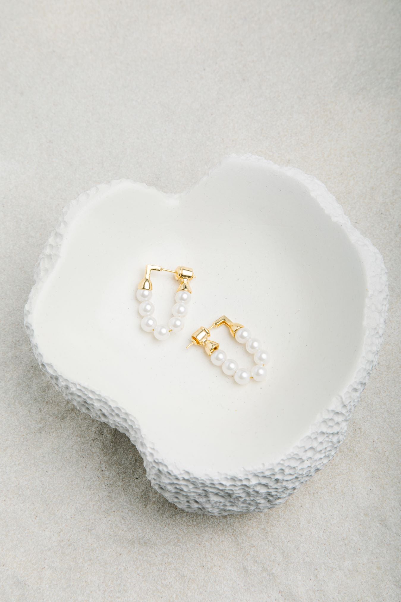 Kristy Earrings displayed in a smooth porcelain bowl with dimpled outer texture, set against a soft felt background in gentle light