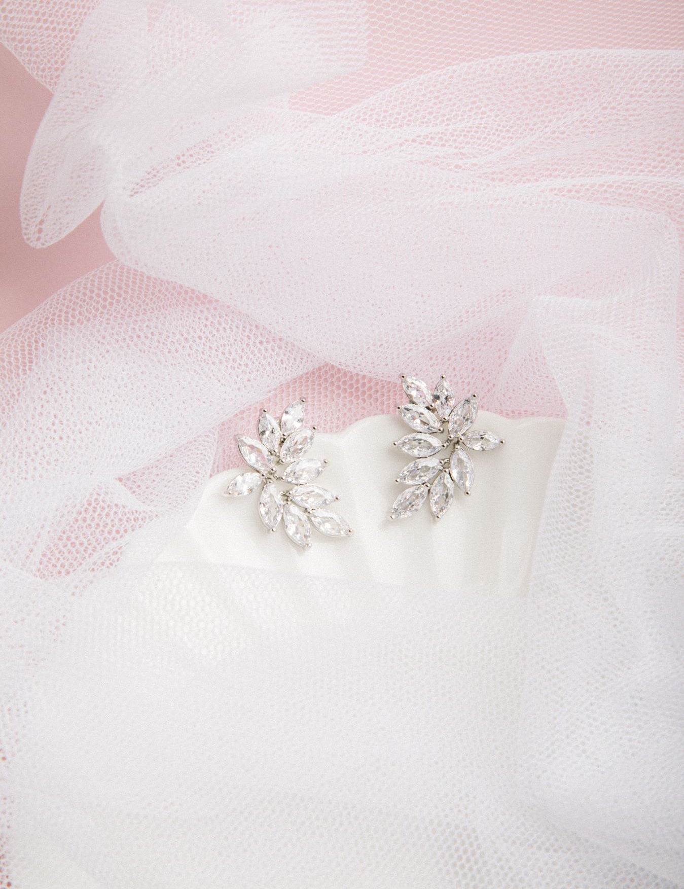 Kya Earrings in silver on a scalloped porcelain plate with soft pink glow and sheer veil in the background