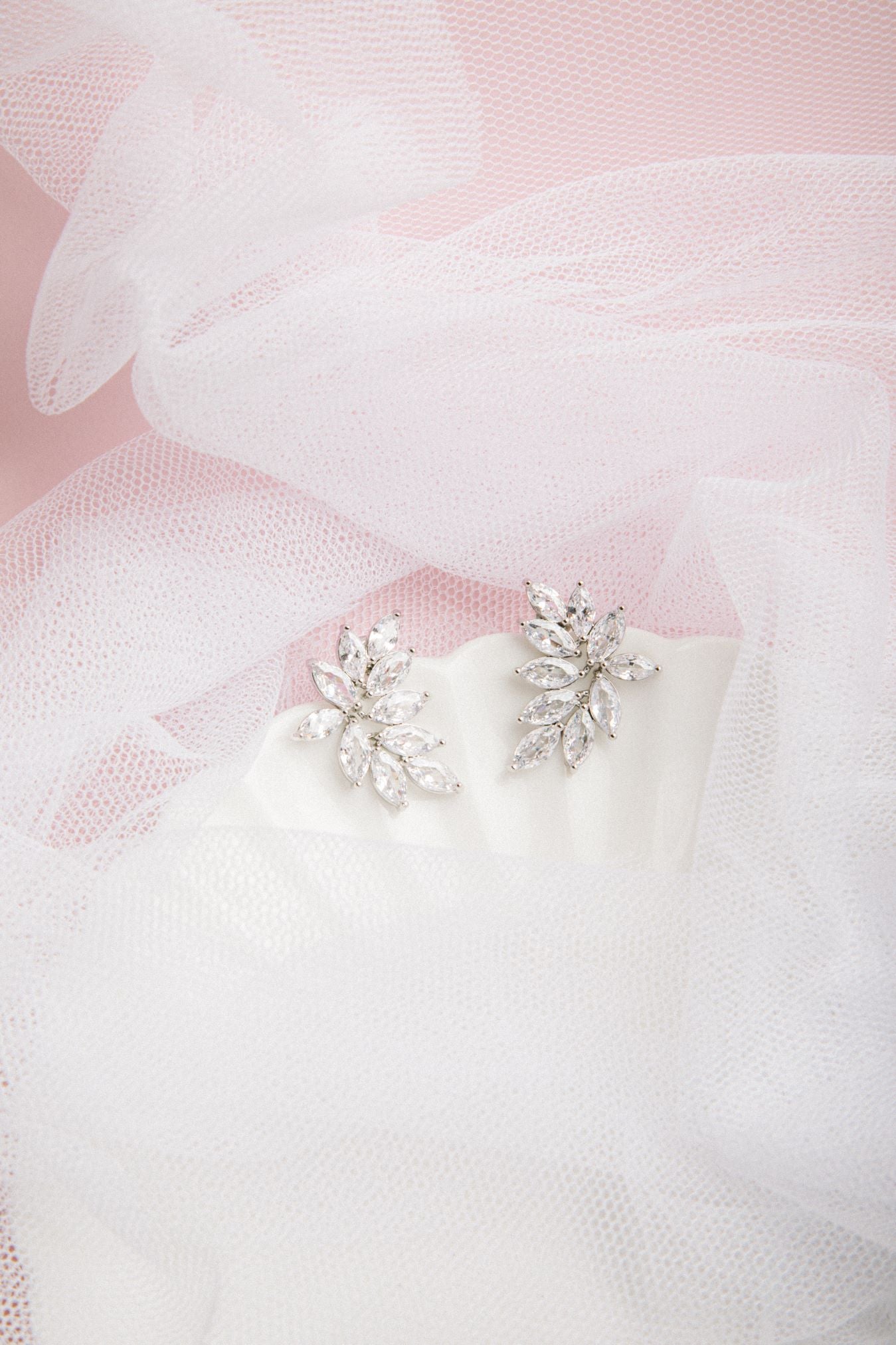 Kya Earrings in silver on a scalloped porcelain plate with soft pink glow and sheer veil in the background