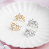 Kya Earrings in gold and silver displayed side by side on a scalloped porcelain plate with a soft pink glow and delicate veil in the background