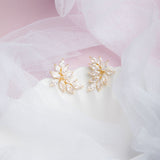 Kya Earrings in gold on a scalloped porcelain plate with soft pink glow and sheer veil in the background