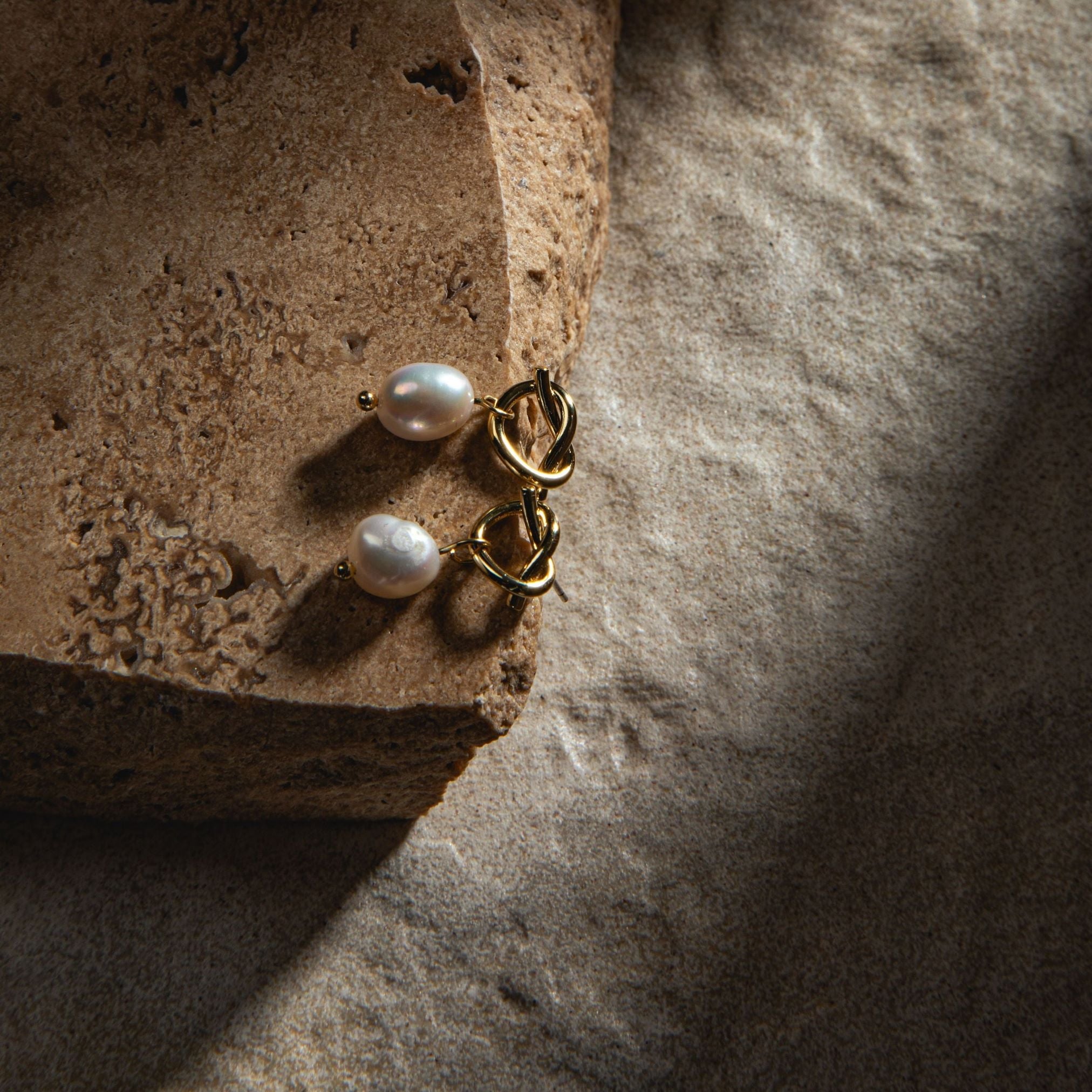 Peyton Earrings in gold – resting on a sandstone paver with dramatic ray of light on a textured sand-coloured background