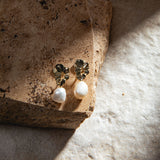 Mini Destiny Earrings in gold – clip-on pearl earrings resting on a brown sandstone paver with a dramatic beam of light on a mottled grey-brown background