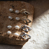 Gold and silver Tiffany Earrings on sandstone paver, illuminated by dramatic light – showing pearl lustre and sculptural metal detailing against a mottled sandy grey-brown background