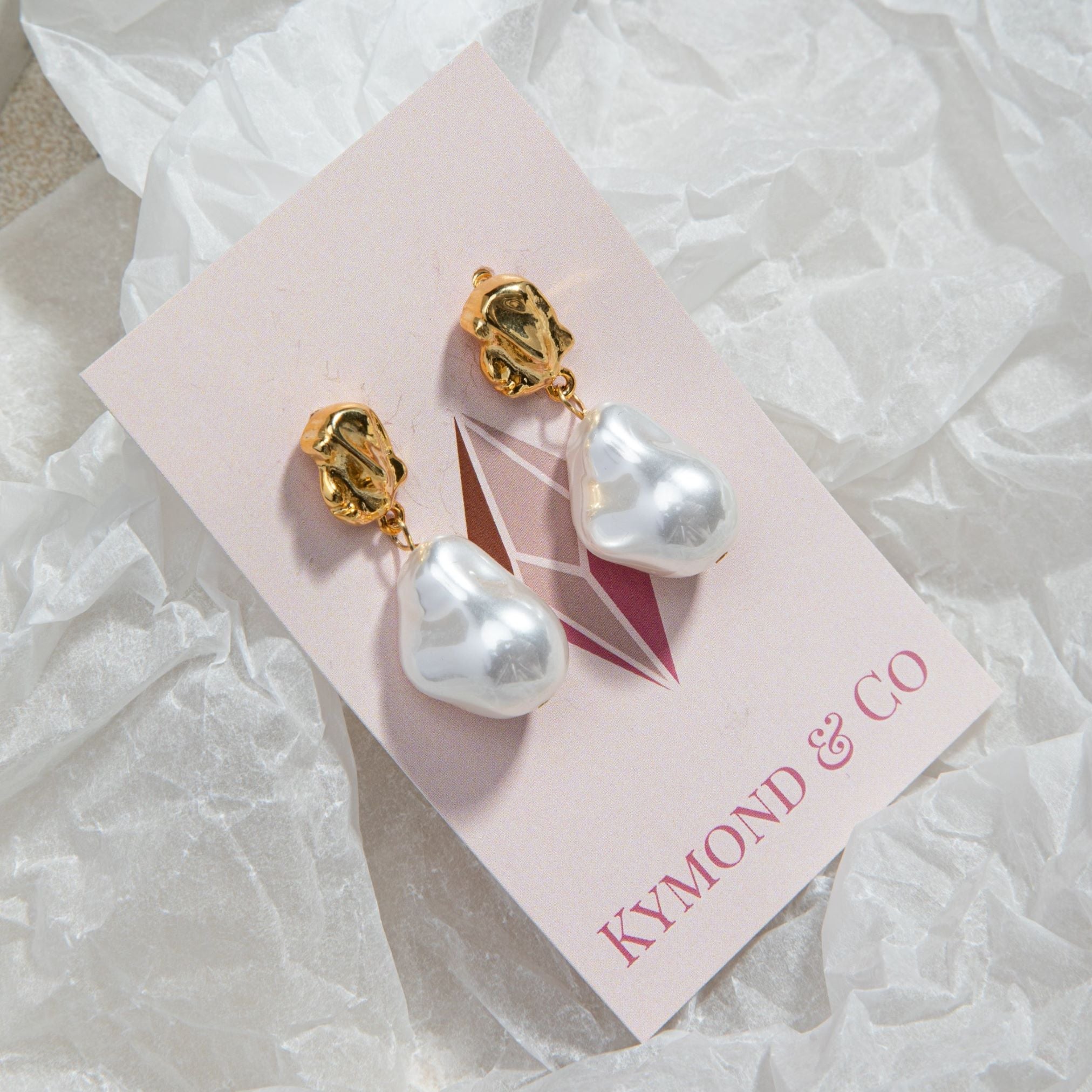 Kat Earrings in gold on Kymond & Co pink card, sitting on crinkled translucent gift wrap paper