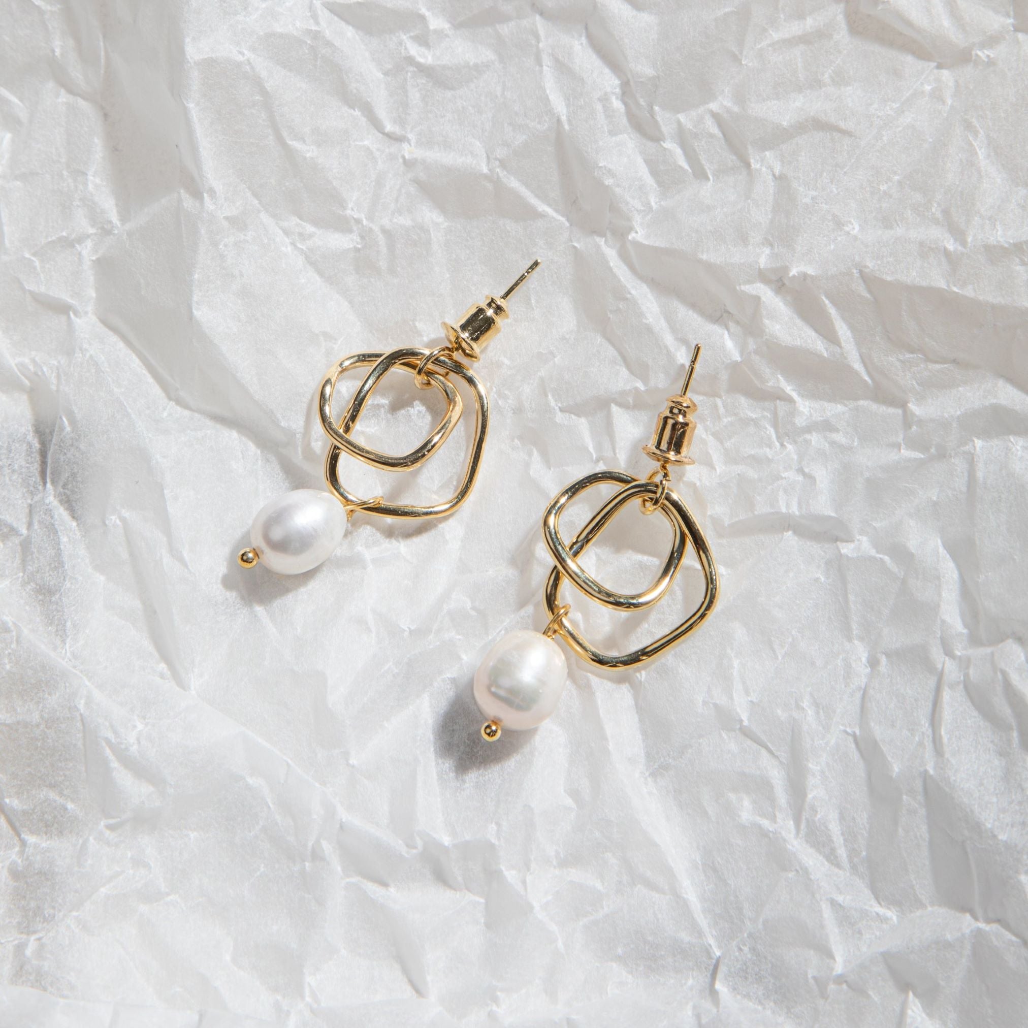 Isabella Earrings – gold twisted hoop earrings with floating pearl on crinkled translucent wrapping paper