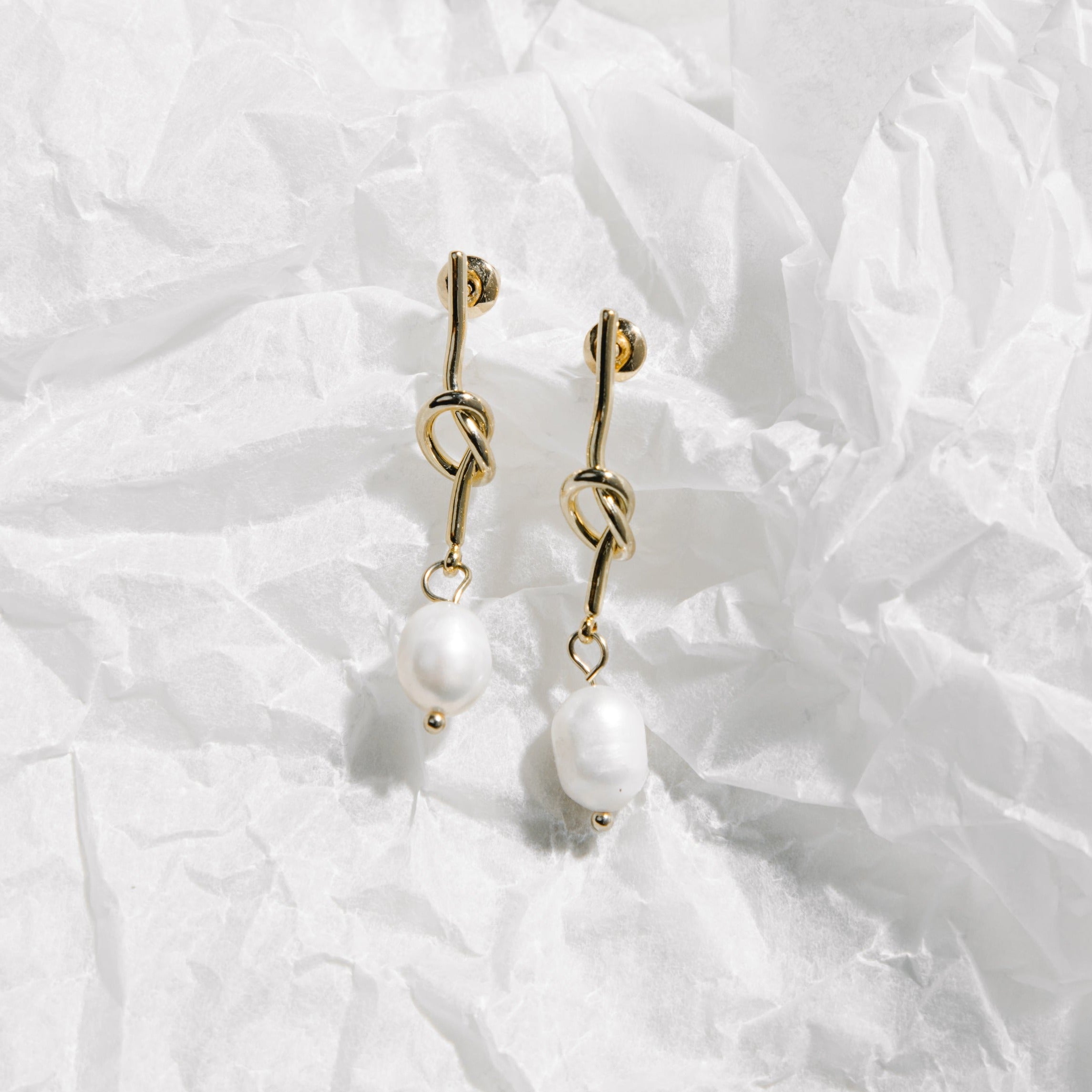 Crystal Earrings – gold knotted pearl drop earrings on crinkled translucent wrapping paper