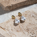 Kat Earrings – freshwater pearl drop earrings in gold on brown pavers and concrete background