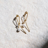 Kiera Earrings – gold dainty knot and pearl stud earrings on textured background