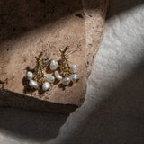 Loretta Earrings – freshwater pearl earrings placed on brown sandstone paver with dramatic lighting and textured felt background