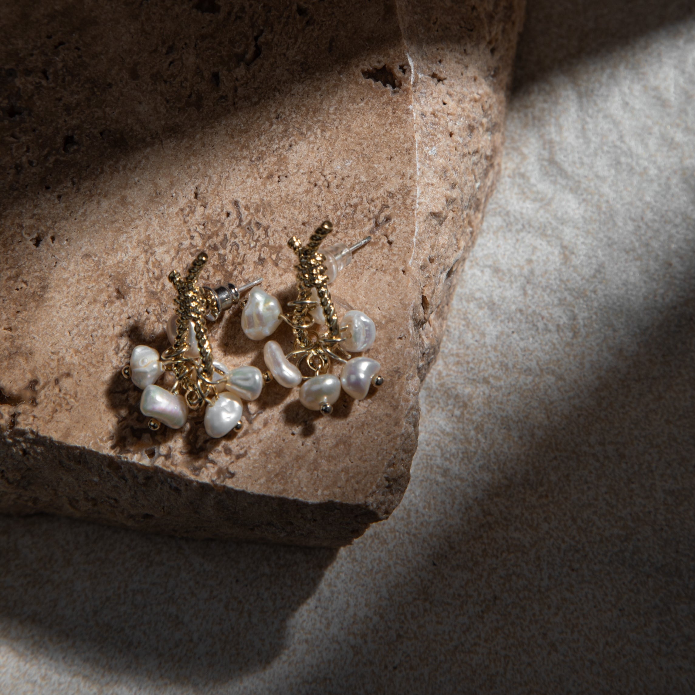 Loretta Earrings – freshwater pearl earrings placed on brown sandstone paver with dramatic lighting and textured felt background