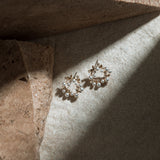 Dainty Flower Earrings – illuminated by a dramatic beam of light on mottled grey-brown background with brown paver alongside