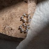 Dainty Flower Earrings – dainty gold floral studs placed on textured brown paver with pearl and crystal detail