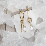 Flatlay of Syntyche Earrings in gold on white tile with sandstone-grey flooring and surrounding wrapping paper