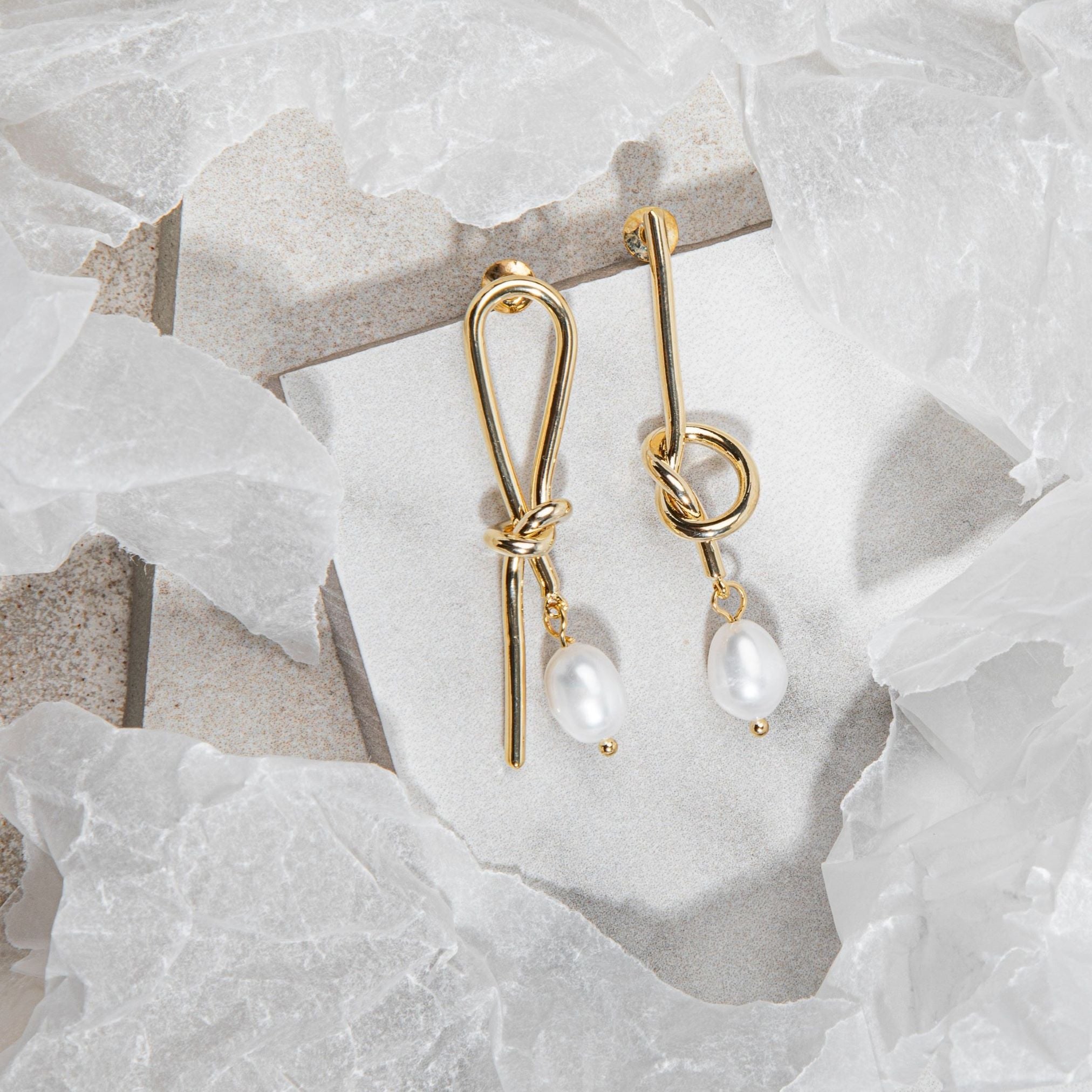 Flatlay of Syntyche Earrings in gold on white tile with sandstone-grey flooring and surrounding wrapping paper