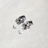 Destiny Earrings – modern gold studs and freshwater pearls resting on textured sand-toned felt surface