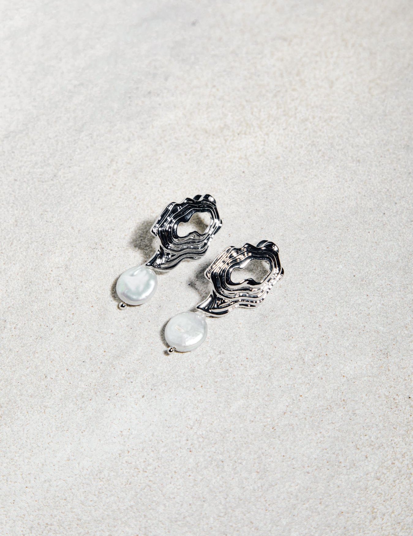 Destiny Earrings – modern gold studs and freshwater pearls resting on textured sand-toned felt surface