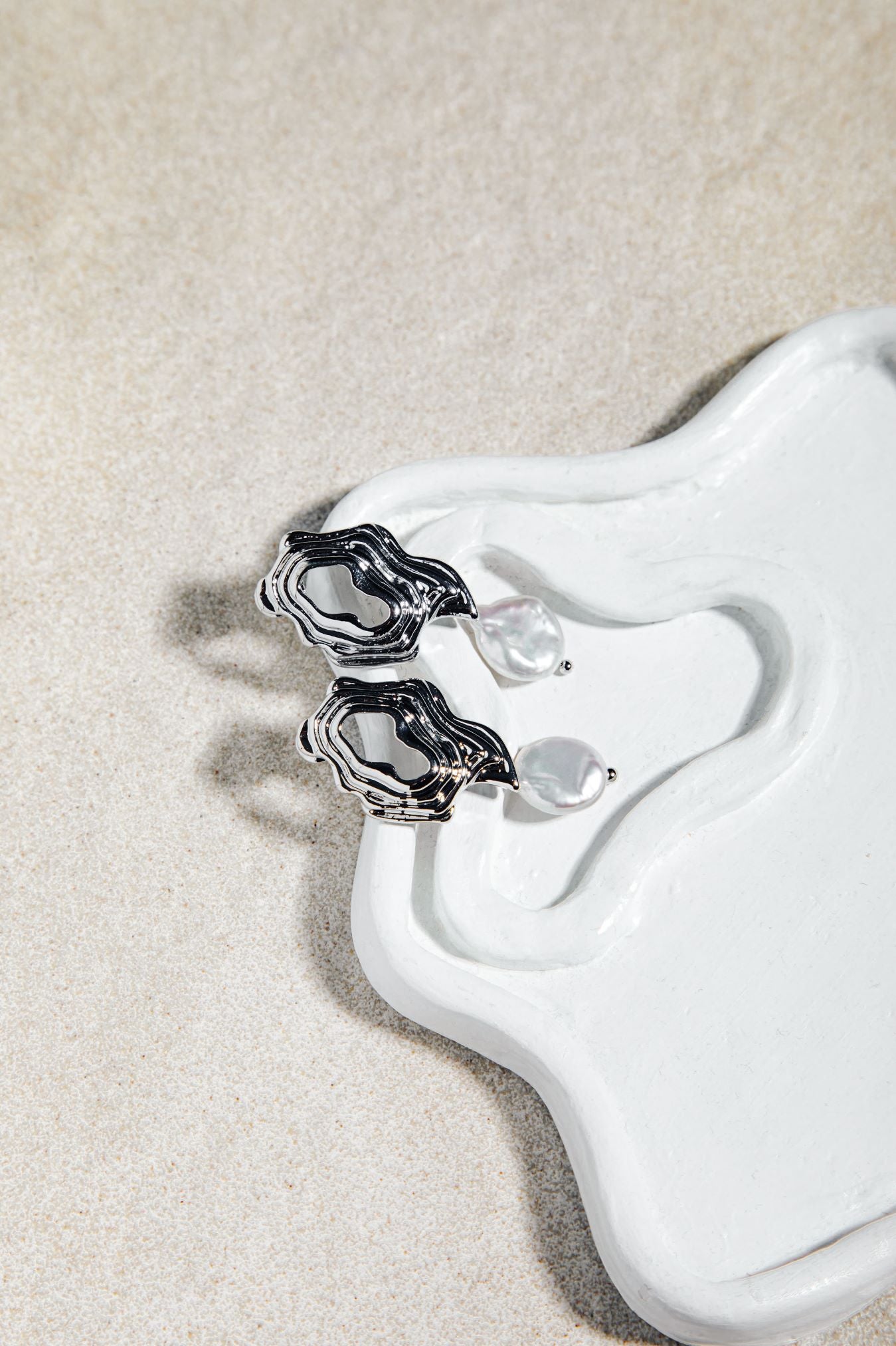 Destiny Earrings – sculptural gold and pearl drop earrings on organic porcelain dish with sand-coloured felt background