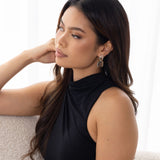 Woman in black dress seated on off-white couch, wearing Bianca Earrings – looking thoughtful with sheer curtains in bright background