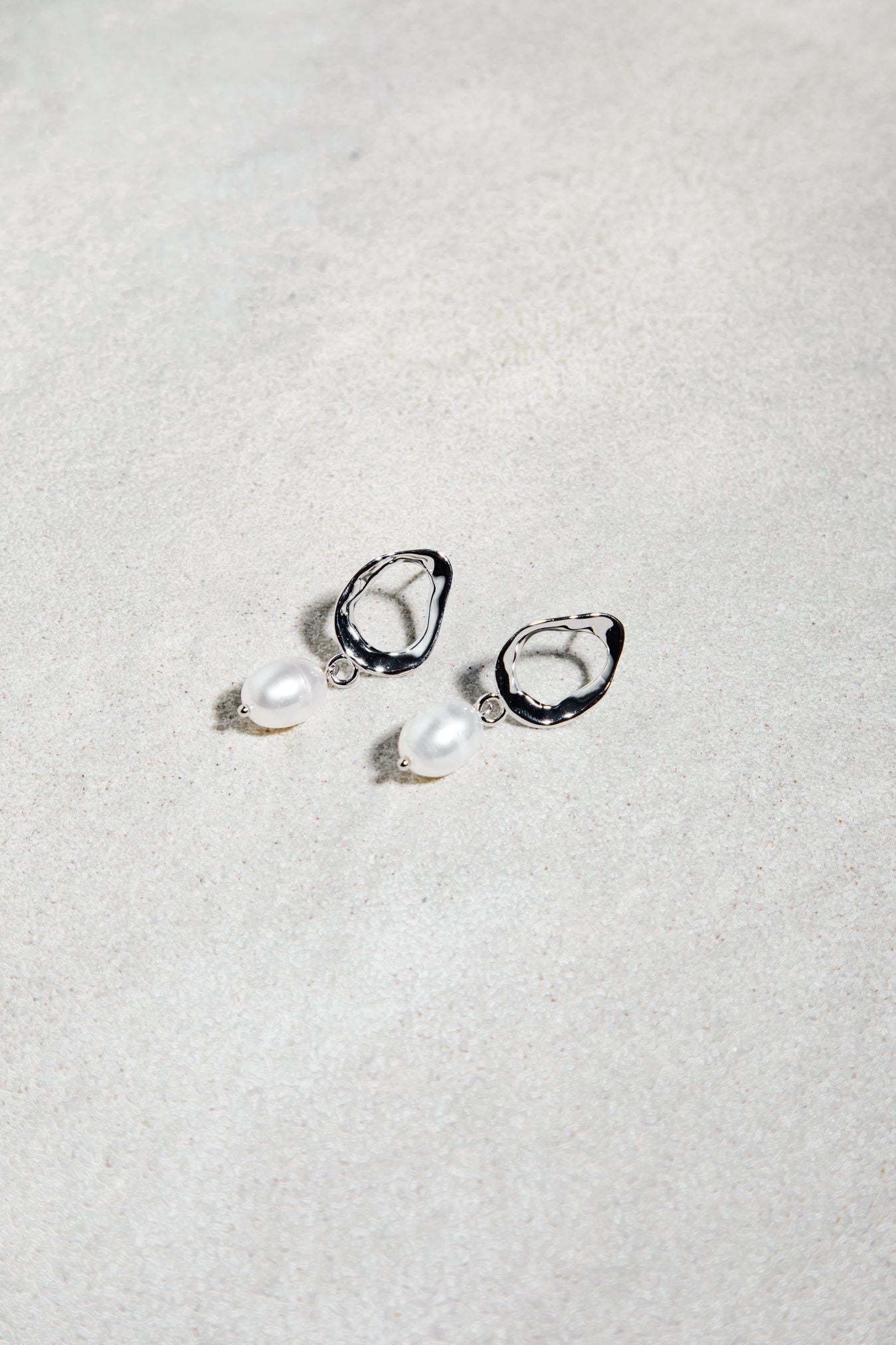 The Sophia Set earrings – silver open hoops with pearl drops on textured surface